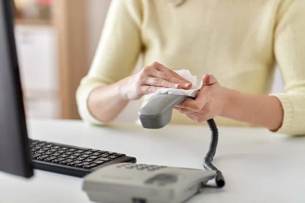 Close up of woman cleaning desk phone with tissue — Stock Photo, Image