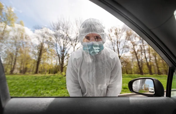 Pracownik służby zdrowia w kombinezonie ochronnym przyglądający się samochodowi — Zdjęcie stockowe