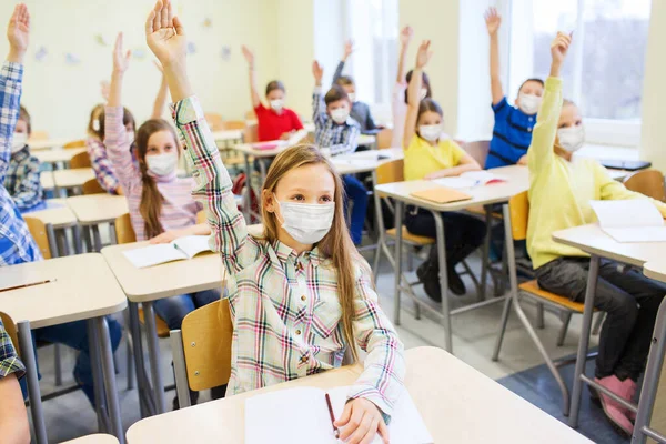 Grupo de estudantes em máscaras levantando as mãos na escola — Fotografia de Stock