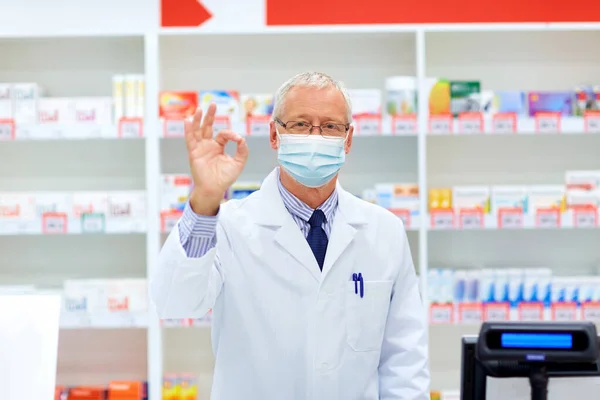 Senior apotheker met masker in de apotheek tonen ok — Stockfoto