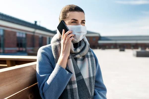 Mujer con máscara facial llamando en el teléfono inteligente en la ciudad Imagen de archivo