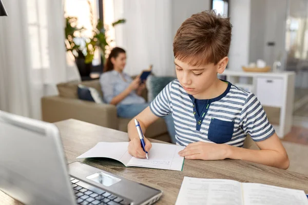 Student boy with book writing to notebook at home — Stock Photo, Image