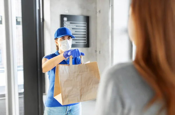 Entrega menina na máscara dando saco de papel ao cliente — Fotografia de Stock