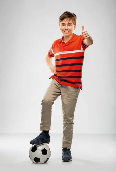 Счастливый мальчик с футбольным мячом, показывающим вверх большие пальцы — стоковое фото
