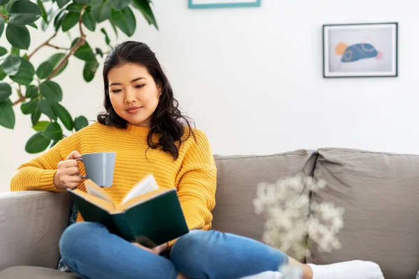 woman reading book and drinking coffee at home
