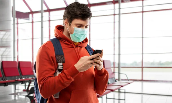 Muž v masce s mobilem a batohem na letišti — Stock fotografie