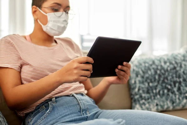 Kvinna i medicinsk mask med tablett dator i hemmet — Stockfoto