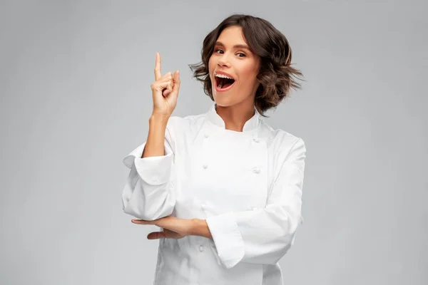 Usmívající se kuchařka v toque ukazující prstem nahoru — Stock fotografie