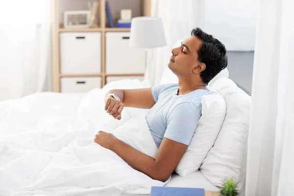 Homem indiano feliz com relógio inteligente na cama em casa — Fotografia de Stock