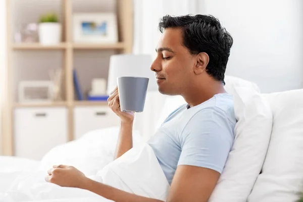Boldog indiai férfi iszik kávét az ágyban otthon — Stock Fotó