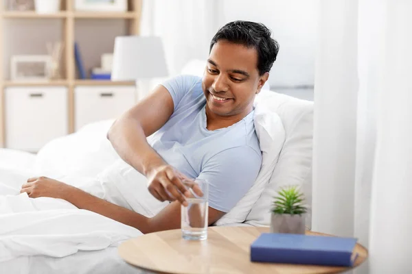 Hombre indio feliz beber agua acostado en la cama —  Fotos de Stock