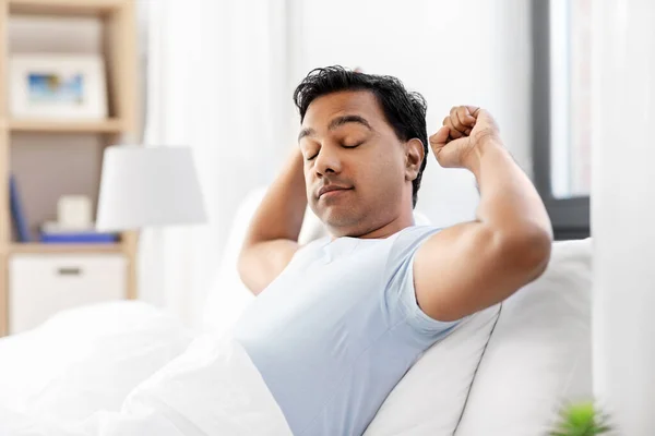 Hombre indio soñoliento estirándose en la cama en casa — Foto de Stock