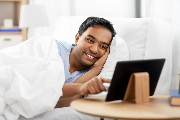 Hombre indio feliz con la tableta PC en la cama en casa —  Fotos de Stock