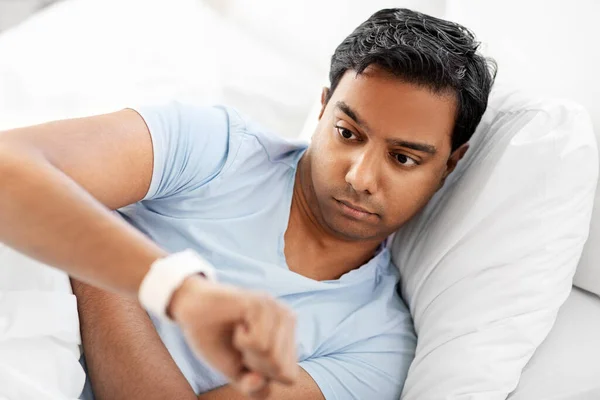 Indian man tittar på smart klocka i sängen hemma — Stockfoto