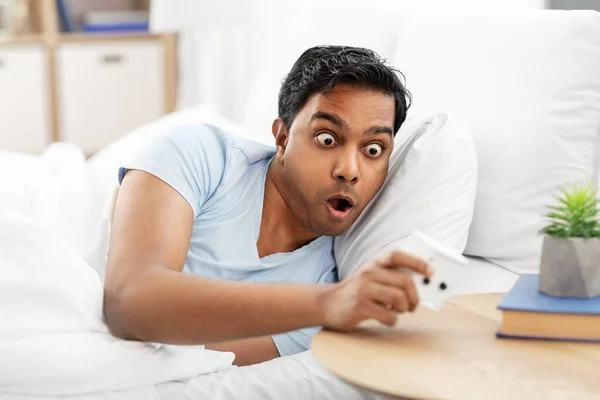 Homem indiano adormecido na cama olhando para despertador — Fotografia de Stock