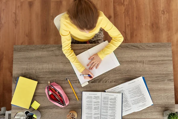 Student flicka med bok skriva till anteckningsbok hemma — Stockfoto