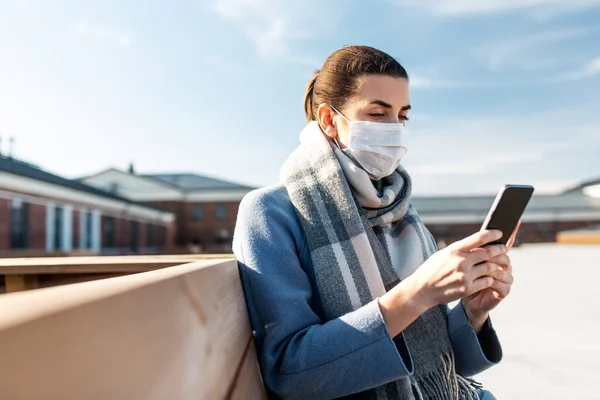 Donna in maschera con smartphone in città — Foto Stock