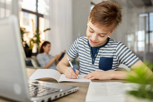 Student pojke med bok skriva till anteckningsbok hemma — Stockfoto