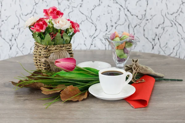 coffee cup with colored candies and flowers on wooden table background