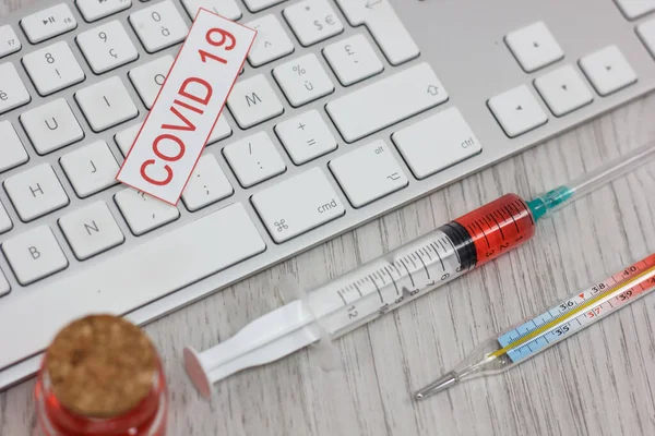 keyboard with medical mask and vaccine with syringe protecting from coronavirus isolated on wooden table background