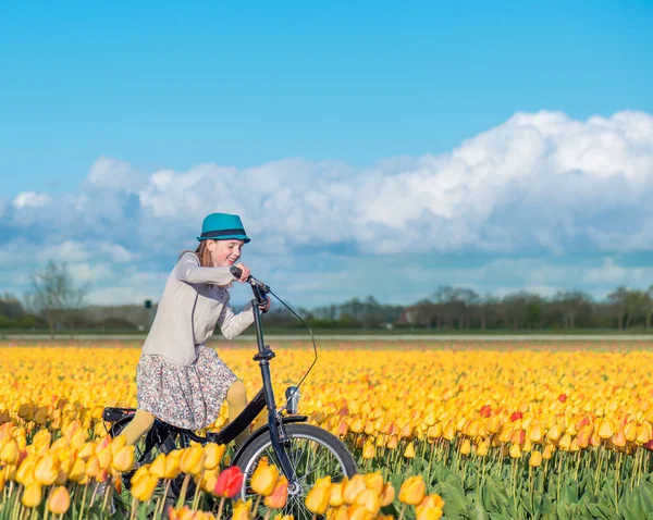 Mulher de pé com sua bicicleta em campos de tulipas — Fotografia de Stock