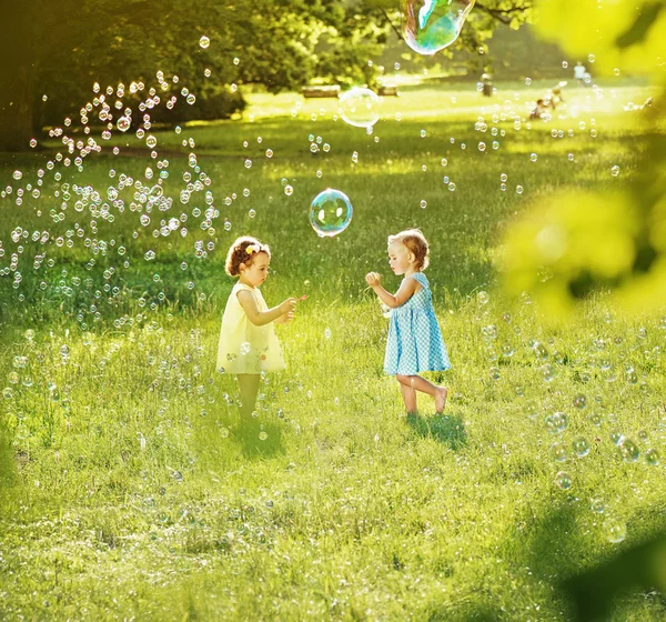 Little girls blowing soap bubbles on a summer meadow — Stock Photo, Image