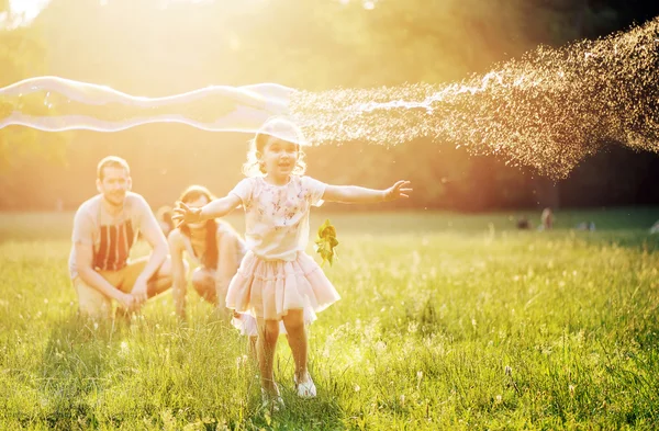 Familia feliz soplando burbujas en un parque de primavera — Foto de Stock