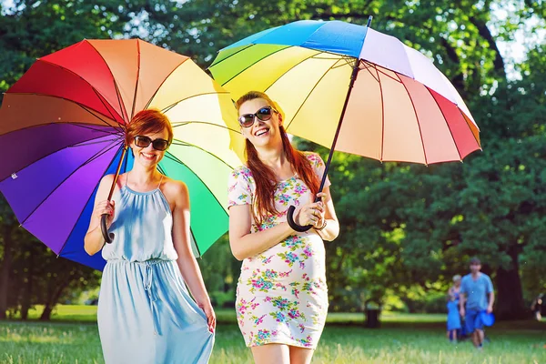 Zwei modische junge Frauen posieren mit bunten Regenschirmen — Stockfoto