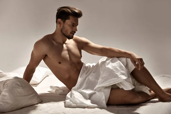 Bonito, homem musculoso posando na cama macia — Fotografia de Stock