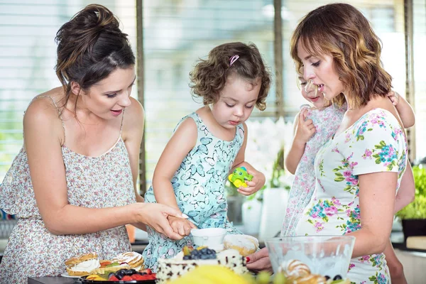 Giovani madri che fanno una torta con le loro figlie — Foto Stock
