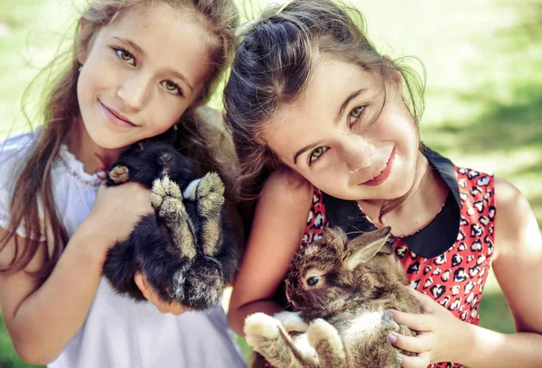 Dos chicas alegres abrazando conejitos esponjosos — Foto de Stock