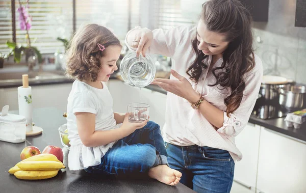 Женщина наполняет стакан водой для своей дочери — стоковое фото