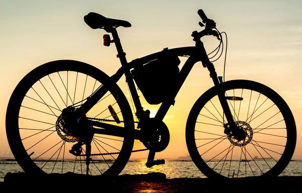 Silhouette of mountain bike at sea with sunset sky background — Stock Photo, Image