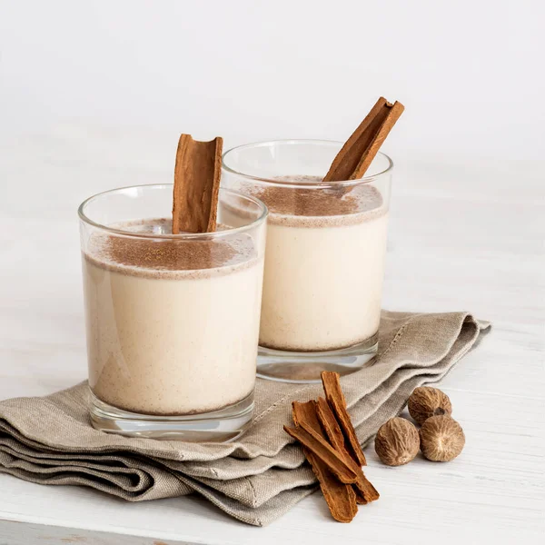 Eggnog in glass cups with a delicate foam, spices and a cinnamon stick — ストック写真