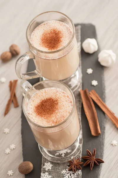 Eggnog in glass cups with a delicate foam, spices and a cinnamon stick — ストック写真