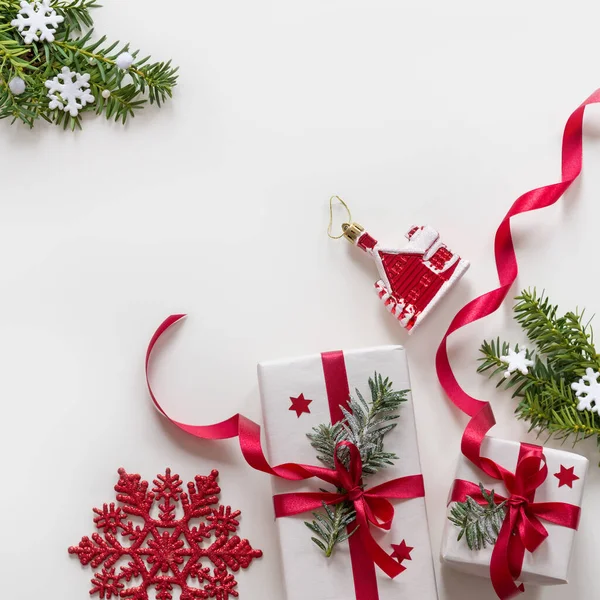 Kırmızı kurdeleli Noel hediyelerinden yapılmış çerçeve, çam dalları, beyaz arka planda oyuncaklar — Stok fotoğraf