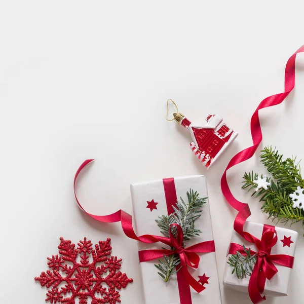 Kırmızı kurdeleli Noel hediyelerinden yapılmış çerçeve, çam dalları, beyaz arka planda oyuncaklar — Stok fotoğraf