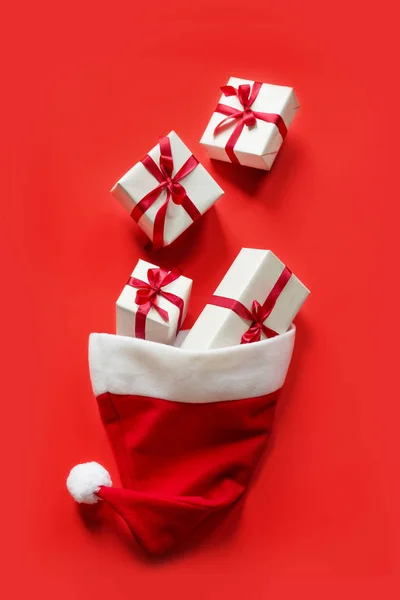 Le chapeau du Père Noël est rempli de boîtes contenant des cadeaux sur fond rouge — Photo
