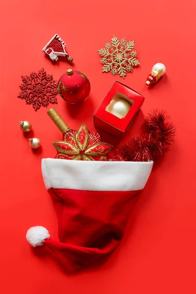 Noel Baba şapkası kırmızı arka planda Noel oyuncaklarıyla dolu. — Stok fotoğraf