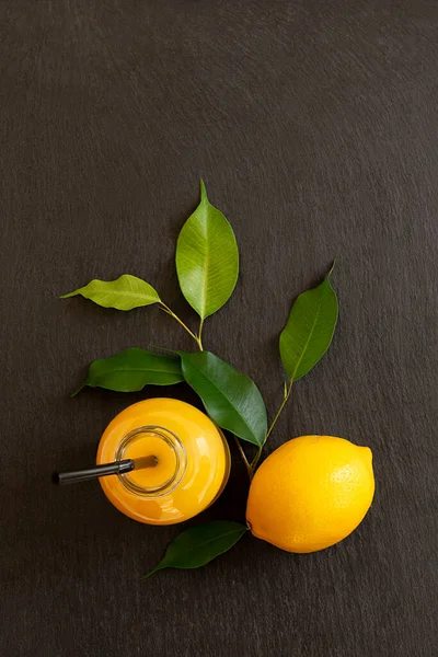 Färska mogna citroner och en flaska med juice på en mörk sten bakgrund — Stockfoto