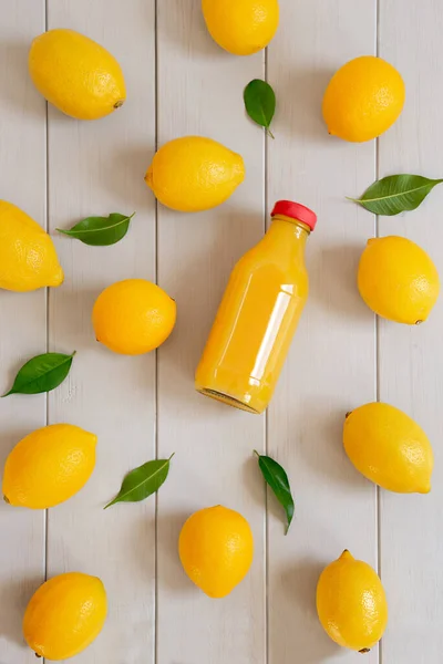 Limoni freschi maturi e una bottiglia con succo su fondo grigio in legno — Foto Stock