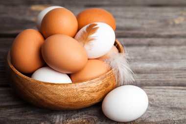 Tahta bir kasede taze beyaz ve kahverengi tavuk yumurtası. Ahşap arka planda çiğ yumurta