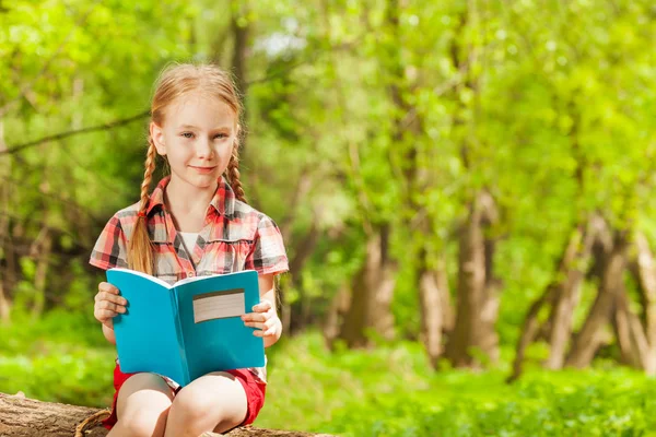 Schoolgirl reading book on log — Stock Photo, Image