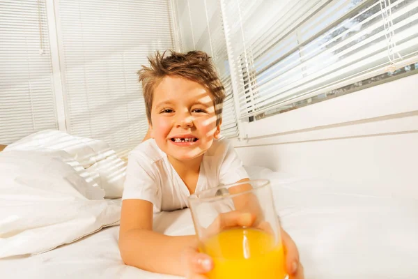 Niño pequeño con vaso de jugo en la cama —  Fotos de Stock