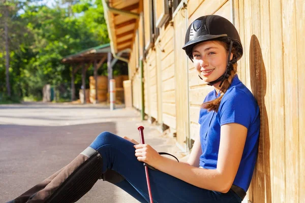 Horsewoman sitting outside a box stall with whip — Stock Photo, Image