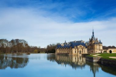 Chateau de Chantilly kalenin doğal görünümü ağaçları bahçeleri ve mavi gökyüzü ile su yansıması