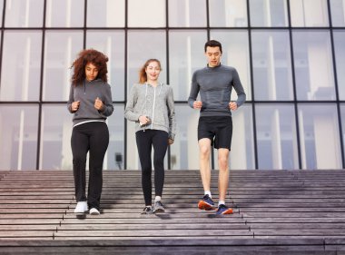 Two young women and one man going downstairs as part of their workout outdoors on city stairs clipart