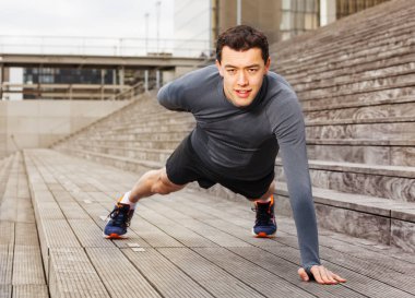 Sporcu içinde gri eşofman açık havada şehirde bir yandan push-up egzersizleri yapıyor