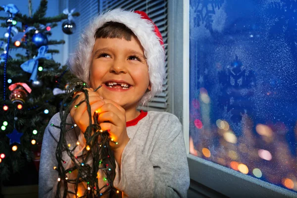 幸せな小さな男の子笑って笑顔と新年のイルミネーションを開催約はクリスマス ツリーの上に置く — ストック写真