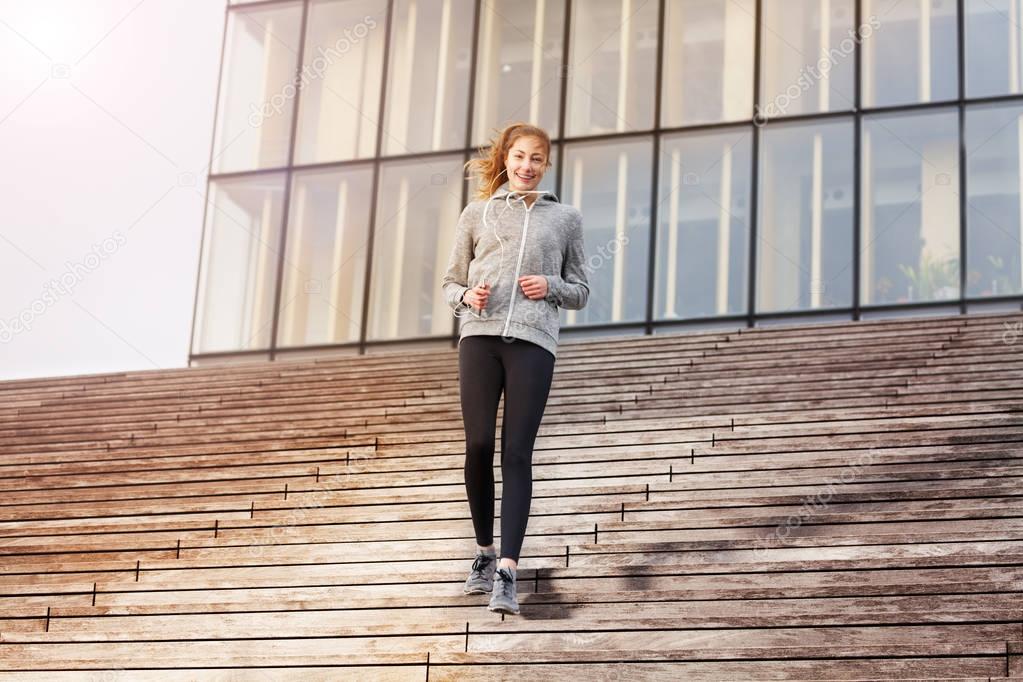 Full-length portrait of happy young woman in sportswear going downstairs as part of her workout outdoors on city stairs